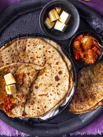 few aloo methi parathas served with pickle and butter.