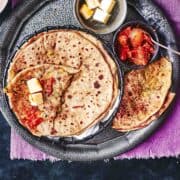 few aloo methi parathas served with pickle and butter.