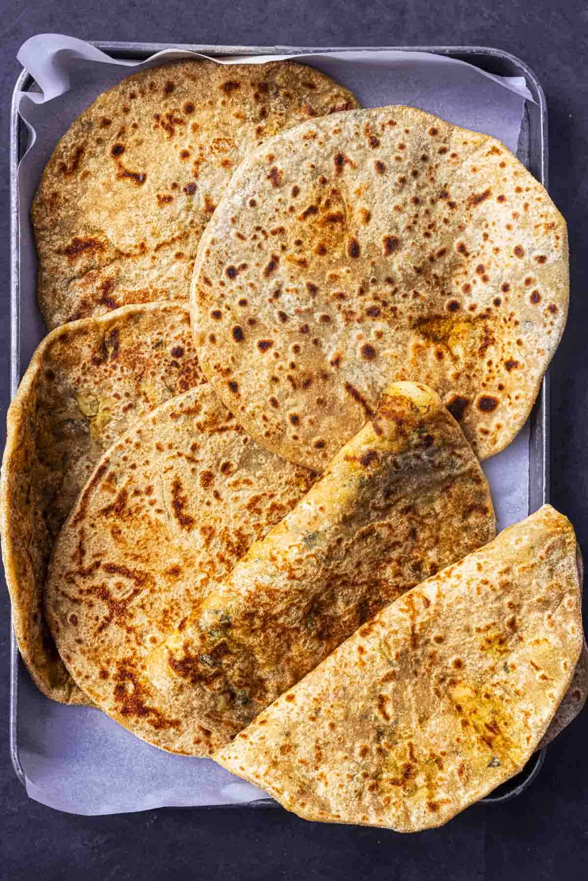 few aloo methi parathas in a baking sheet lined with parchment paper.