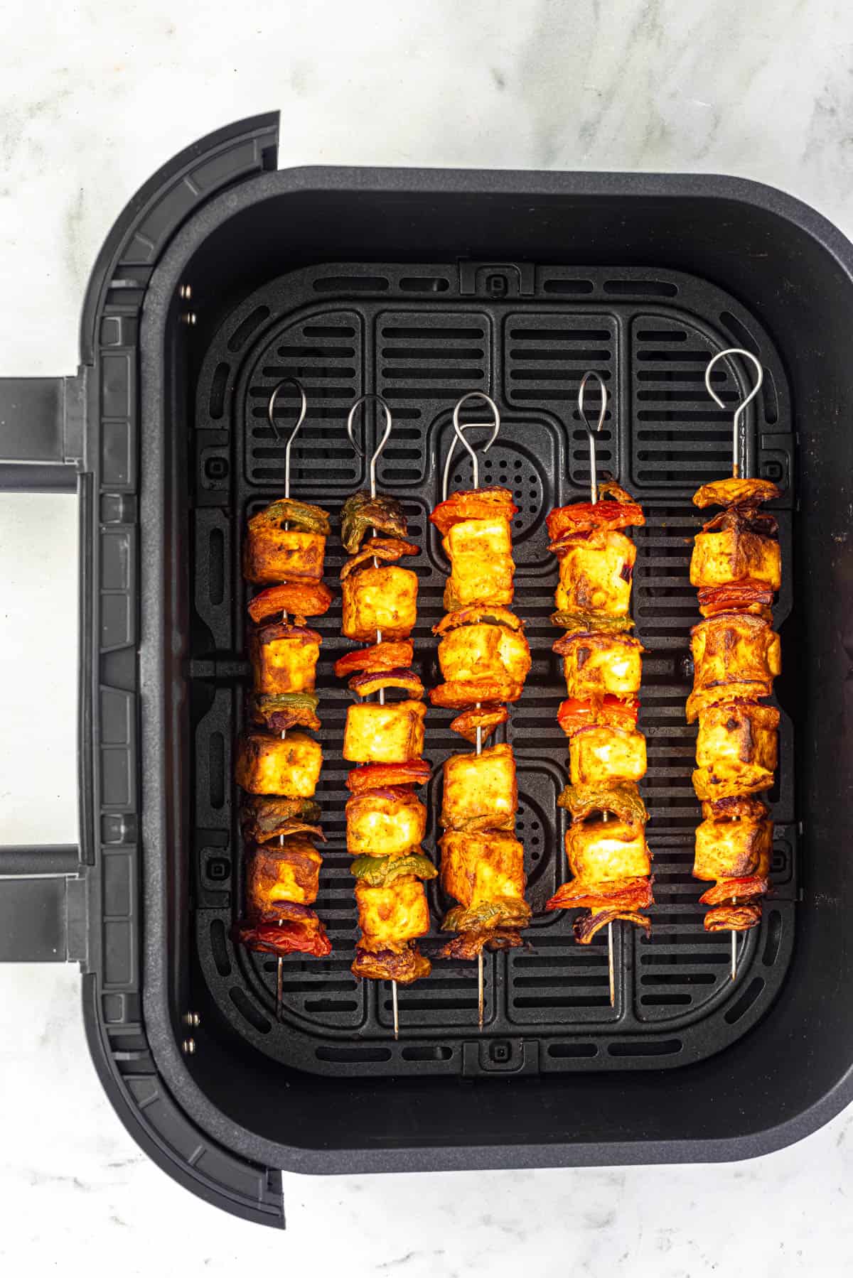 air fryer paneer tikka skewers in air fryer basket.