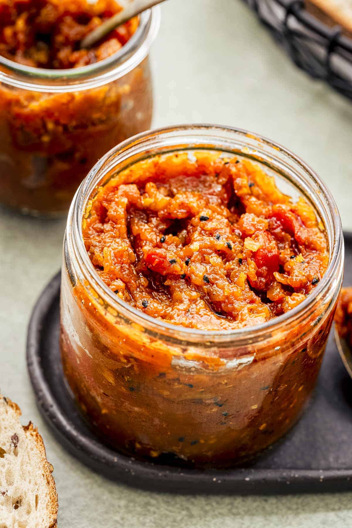 two jars of bright apple chutney served with bread.