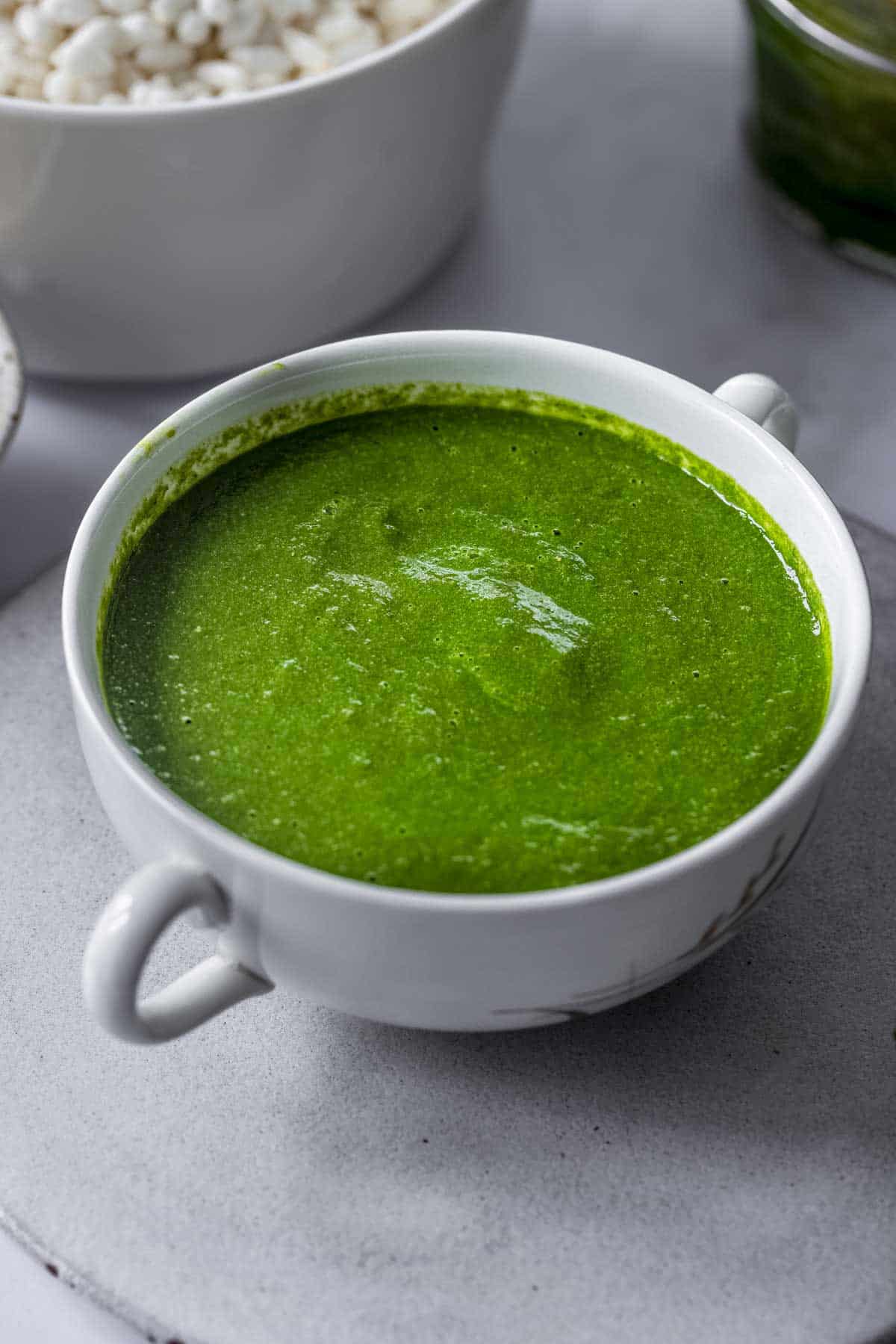 a bowl of green coriander chutney. there is a bowl of rice puffs also known as bhel at the back.
