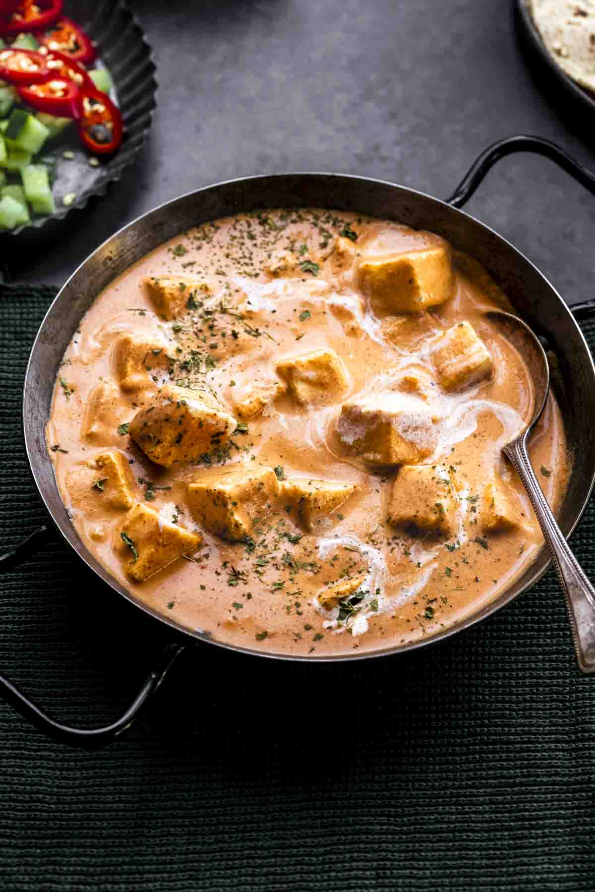 paneer makhani in a serving dish with two handles and chopped salad on the side.