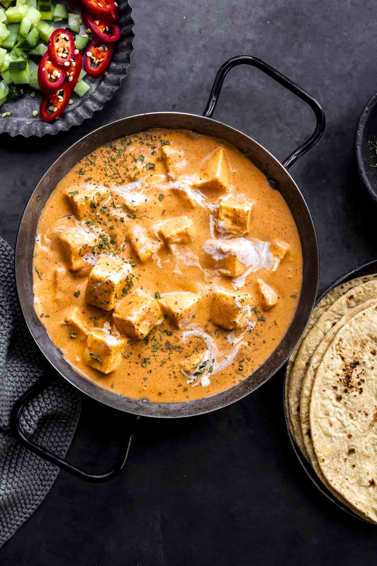 paneer makhani in a serving dish with two handles with chapatis and salad on the side.