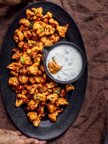 a black platter full of buffalo cauliflower wings serve with ranch dip.