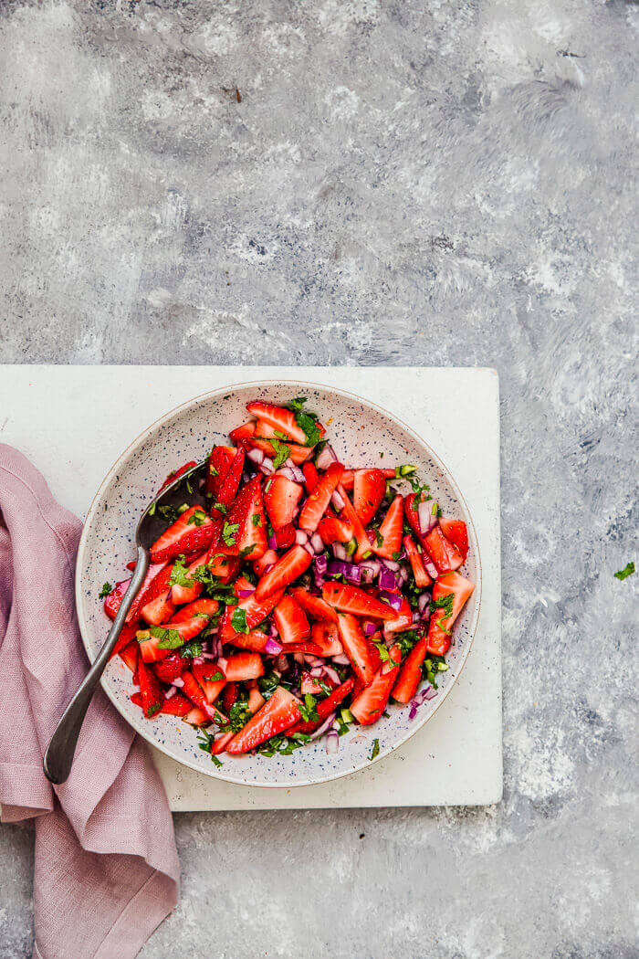 A bowl of strawberries salsa on a grey background.