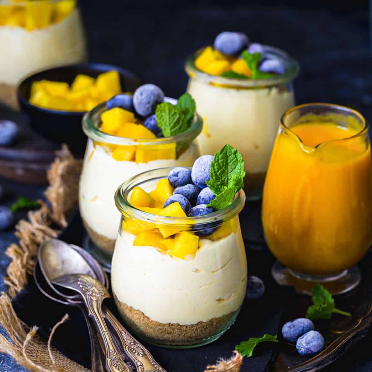o bake mango cheesecake cups in glass jars topped with fresh mango cubes, blueberry and mint.