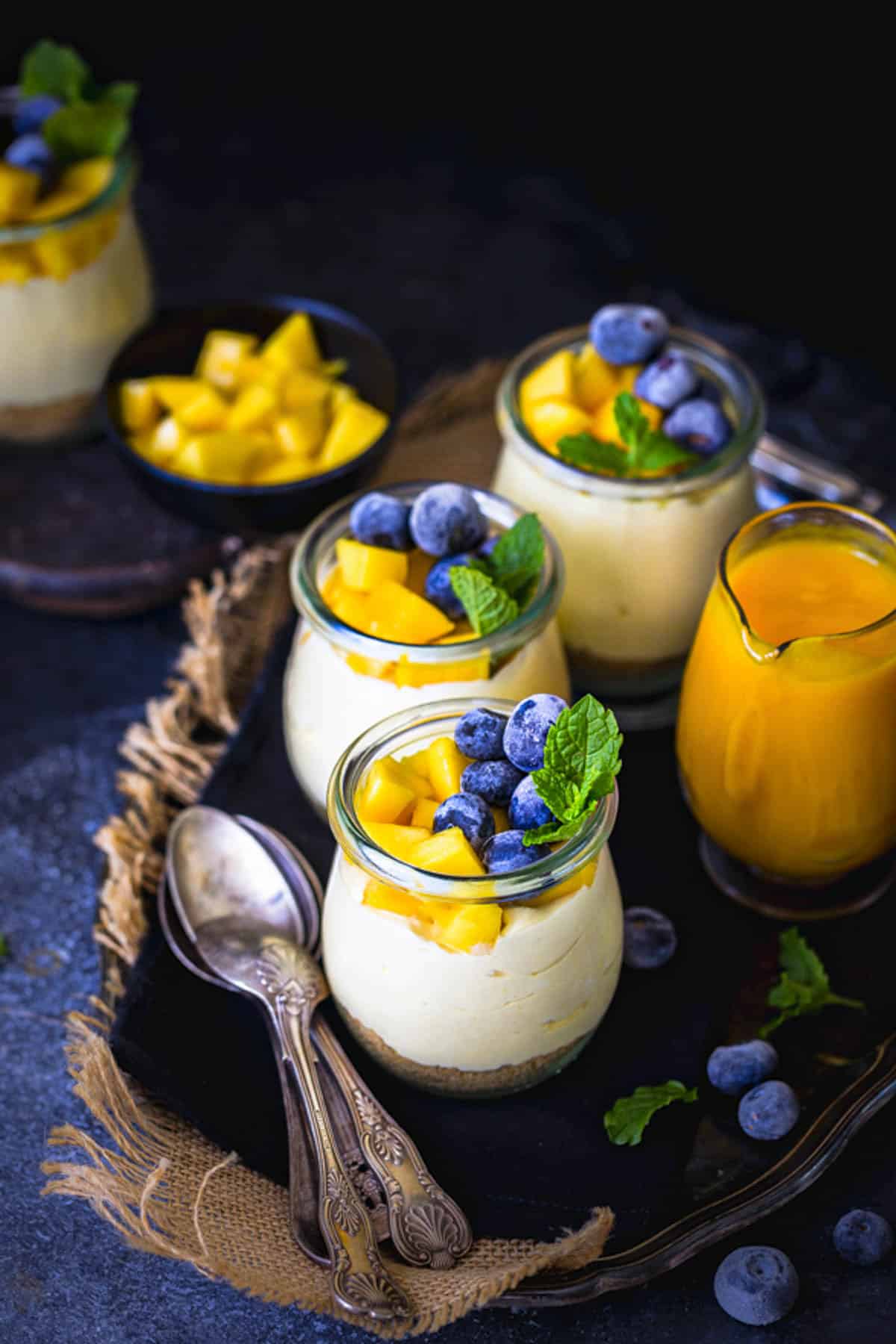 Creamy eggless mango cheesecake cup with biscuit base and mango topping.