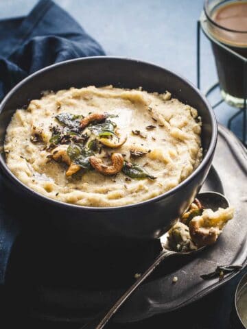 rava pongal served in a black bowl and two cups of tea in the background.