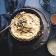rava pongal served in a black bowl with a spoon scooped in and two cups of tea in the background.