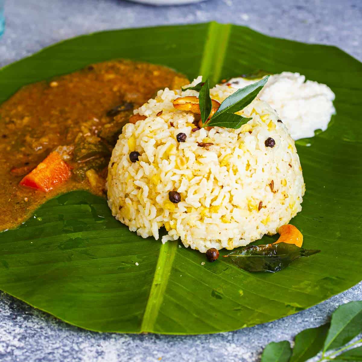 ven pongal served on a banana leaf with sambar and coconut chutney