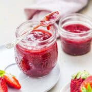 fresh strawberry jam in two jam jars with strawberries in the background.