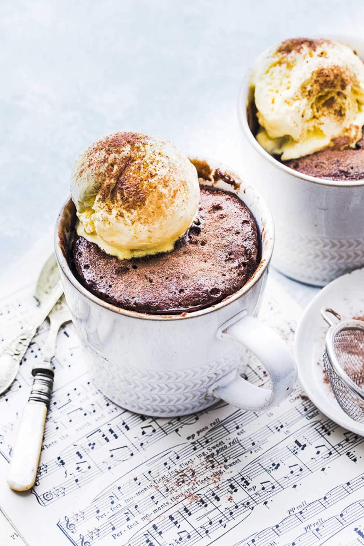 Two white mugs hold Nutella mug cake topped with ice cream.