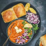 Pav Bhaji topped with onions, butter, coriander, and lemon, served with soft eggless dinner rolls.