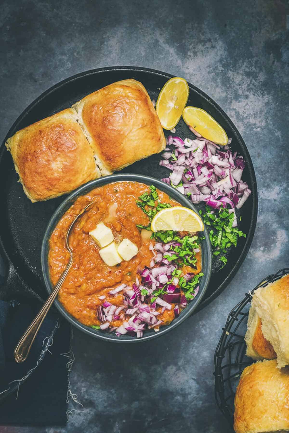 Pav Bhaji topped with onions, butter, coriander, and lemon, served with soft eggless dinner rolls.