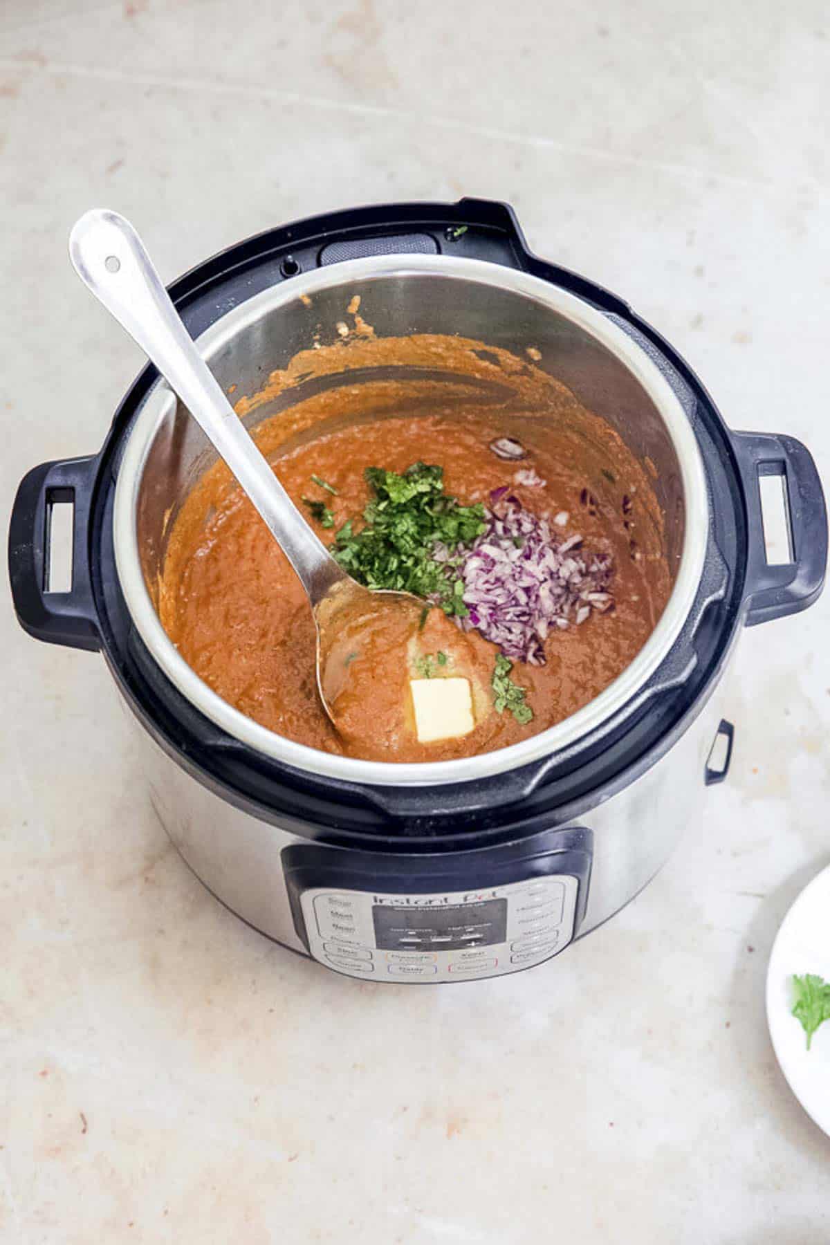 finished pav bhaji with butter, chopped onion and coriander leaves and a ladle in instant pot.