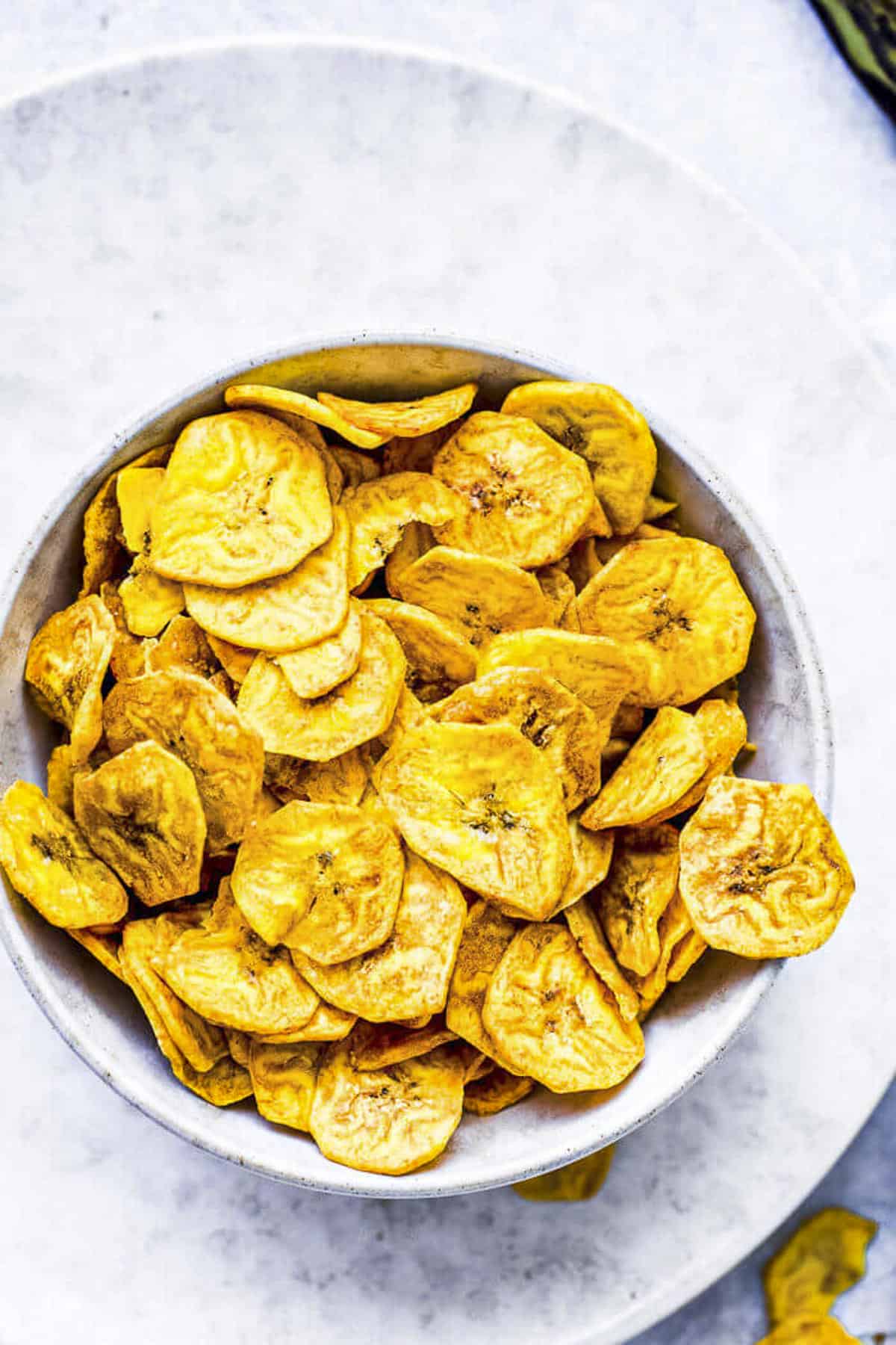 a white bowl of crispy air fryer plantain chips.