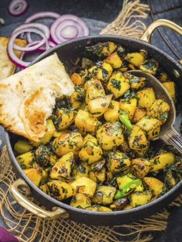 aloo methi served with a slice of naan bread.