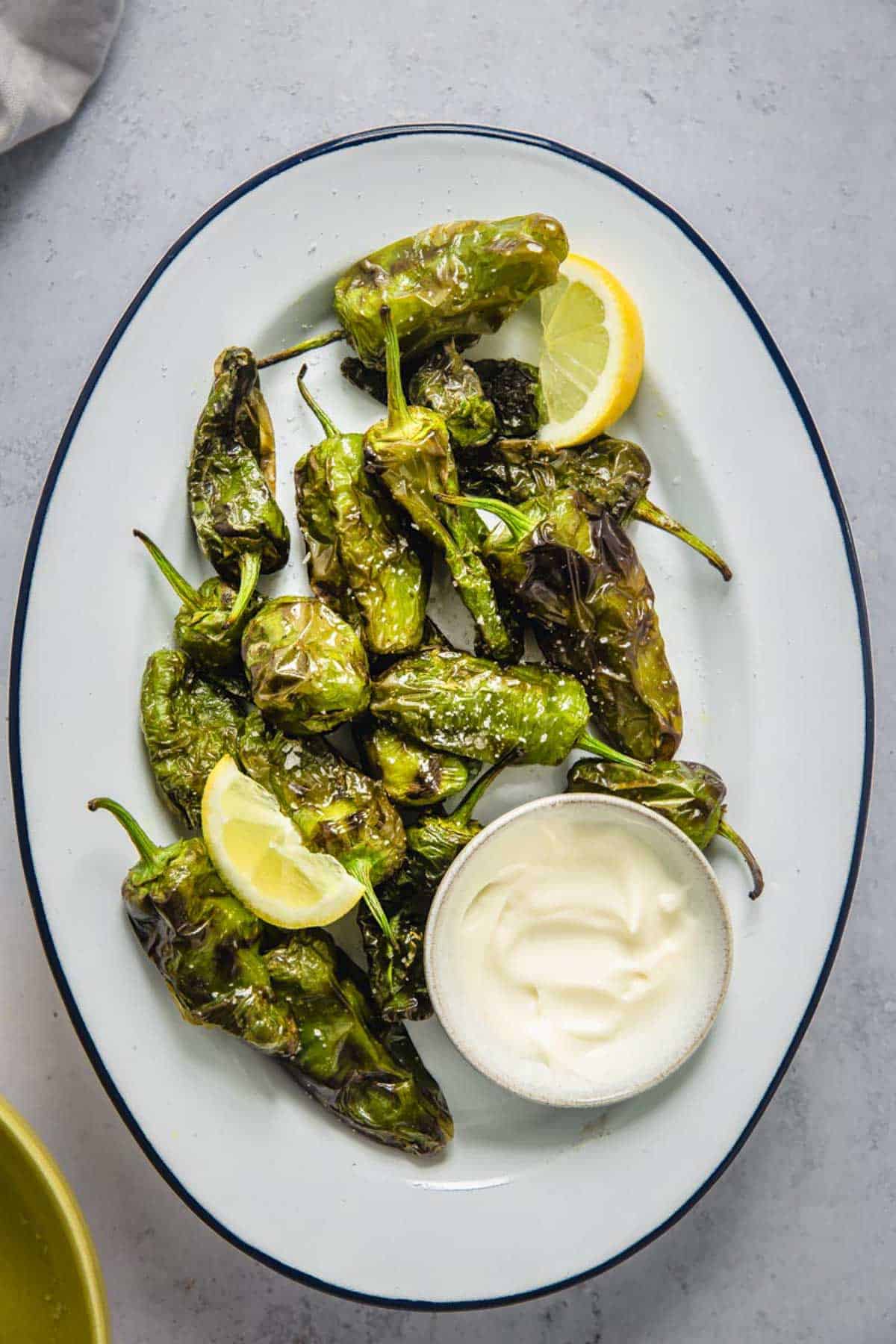 air fried shishito peppers on a oval plate served with a garlic dip.