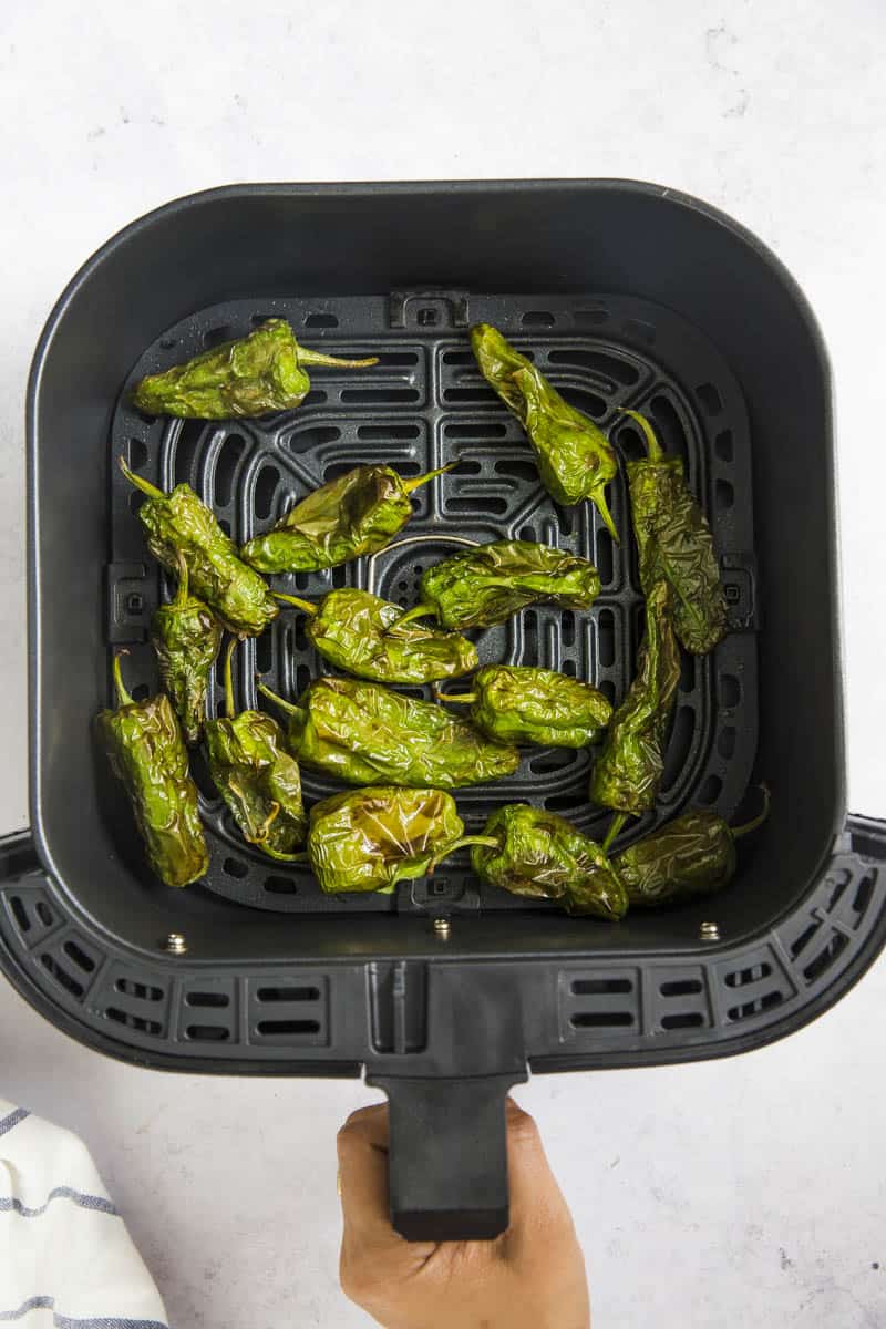air fried shishito peppers in the air fryer basket.