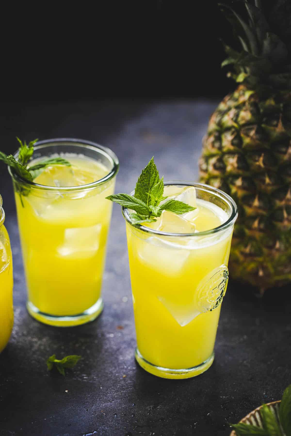 three glasses of pineapple juice served with mint leaves and ice.