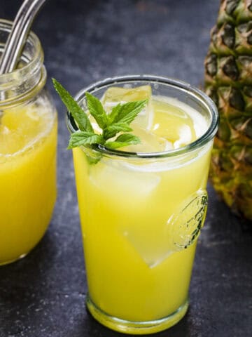 two cups of homemade pineapple juice served over ice and with fresh mint leaves.