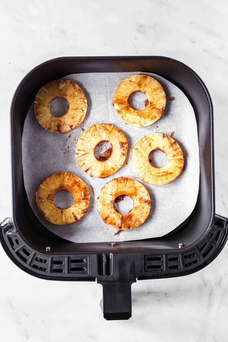 pineapple slices coated with sugar mixture marinade in air fryer basket.