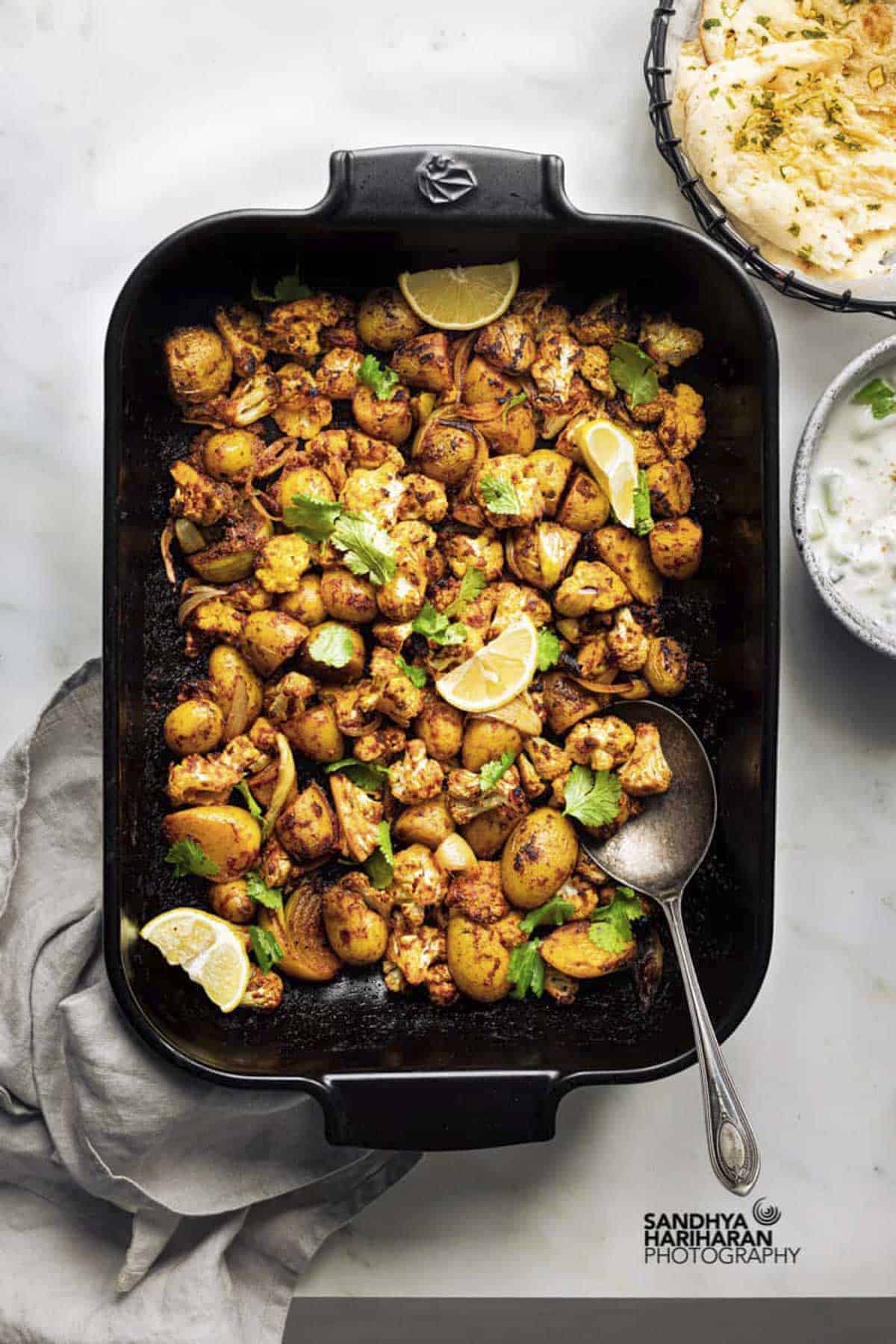 Indian potato cauliflower traybake served with naan and raita.