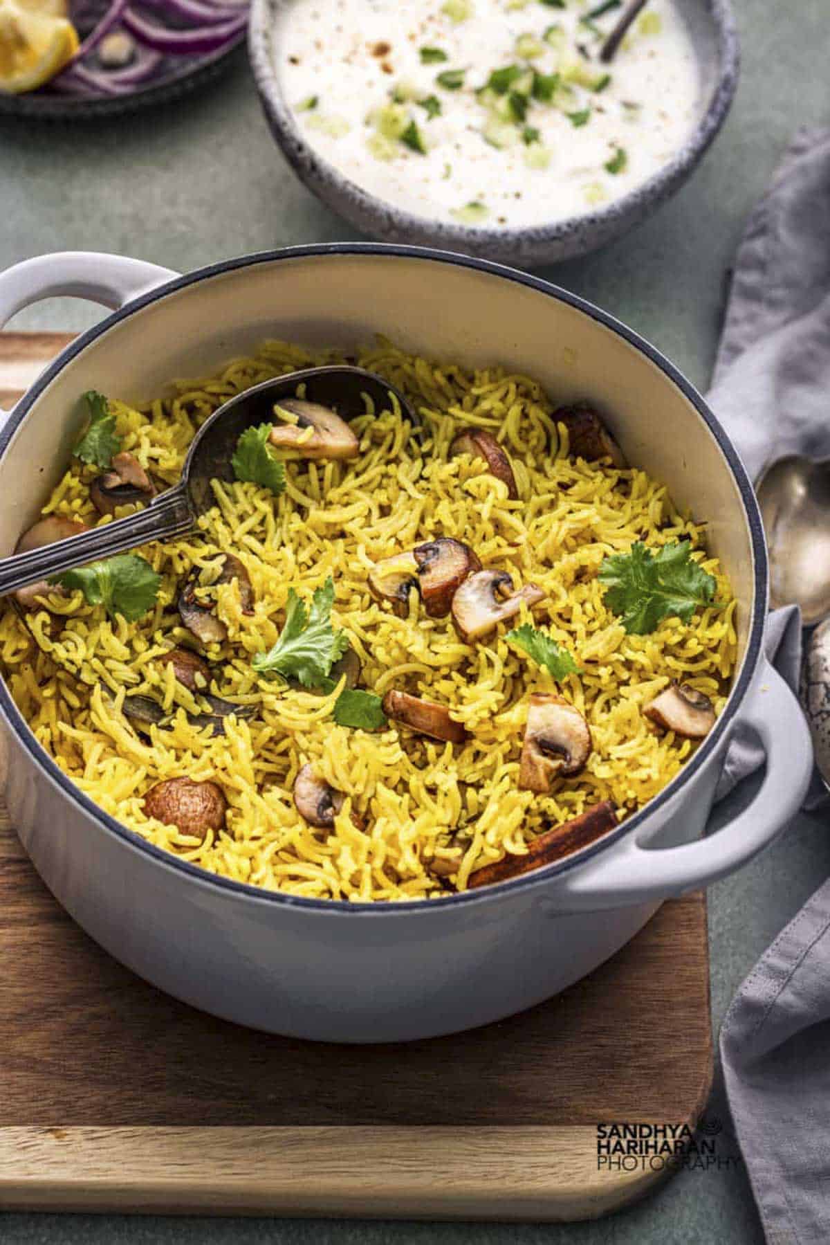 Indian mushroom pilau rice served in a white cast iron pan with raita.