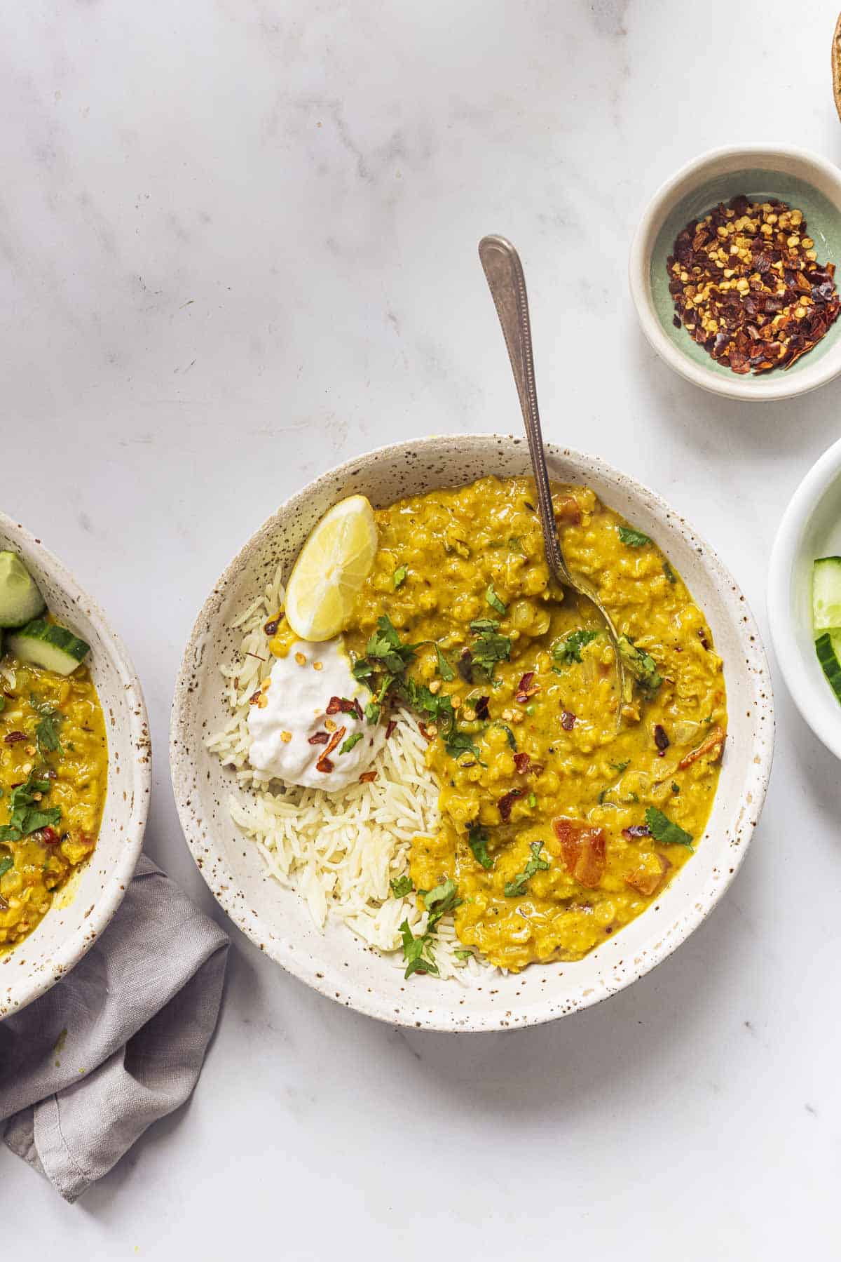 two bowls of red lentil dahl with lemon, chilli flakes, cucumber and yogurt.