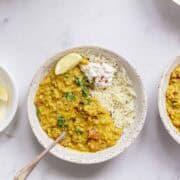 two bowls of red lentil dahl served with cumin rice in white bowls.