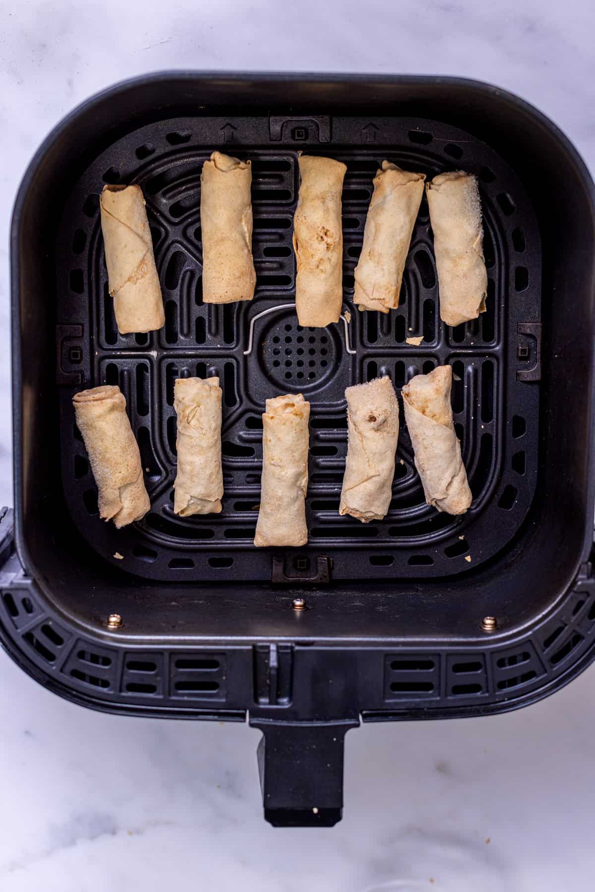frozen spring rolls in air fryer basket.