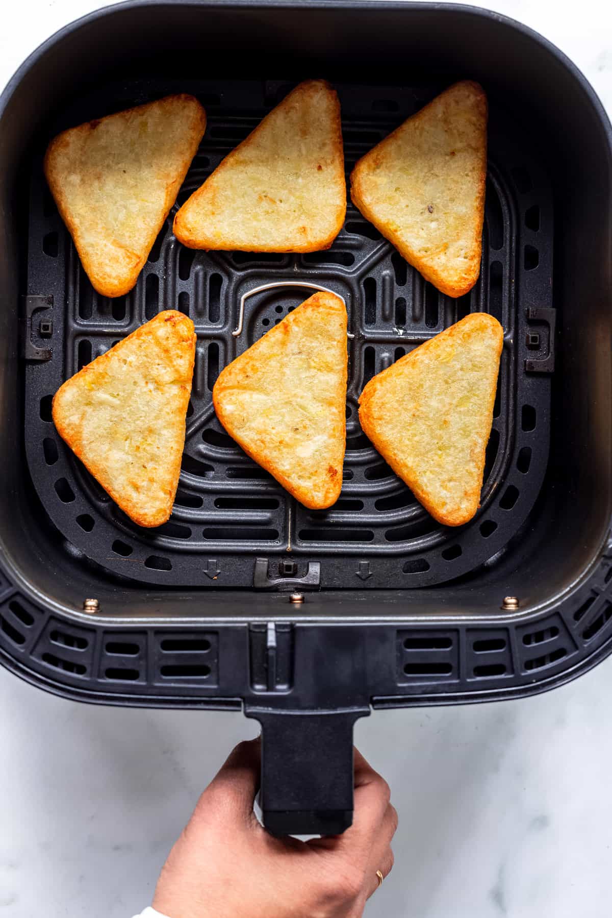 6 cooked hash browns in air fryer basket.