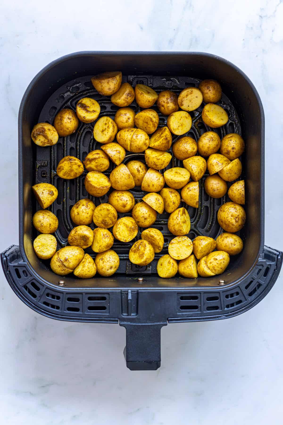 spice coated potatoes in air fryer basket.