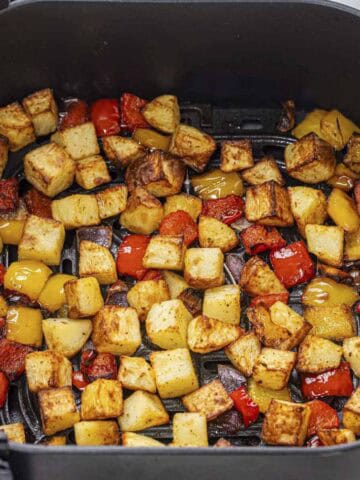 breakfast potatoes with red bell peppers and onions in air fryer basket.
