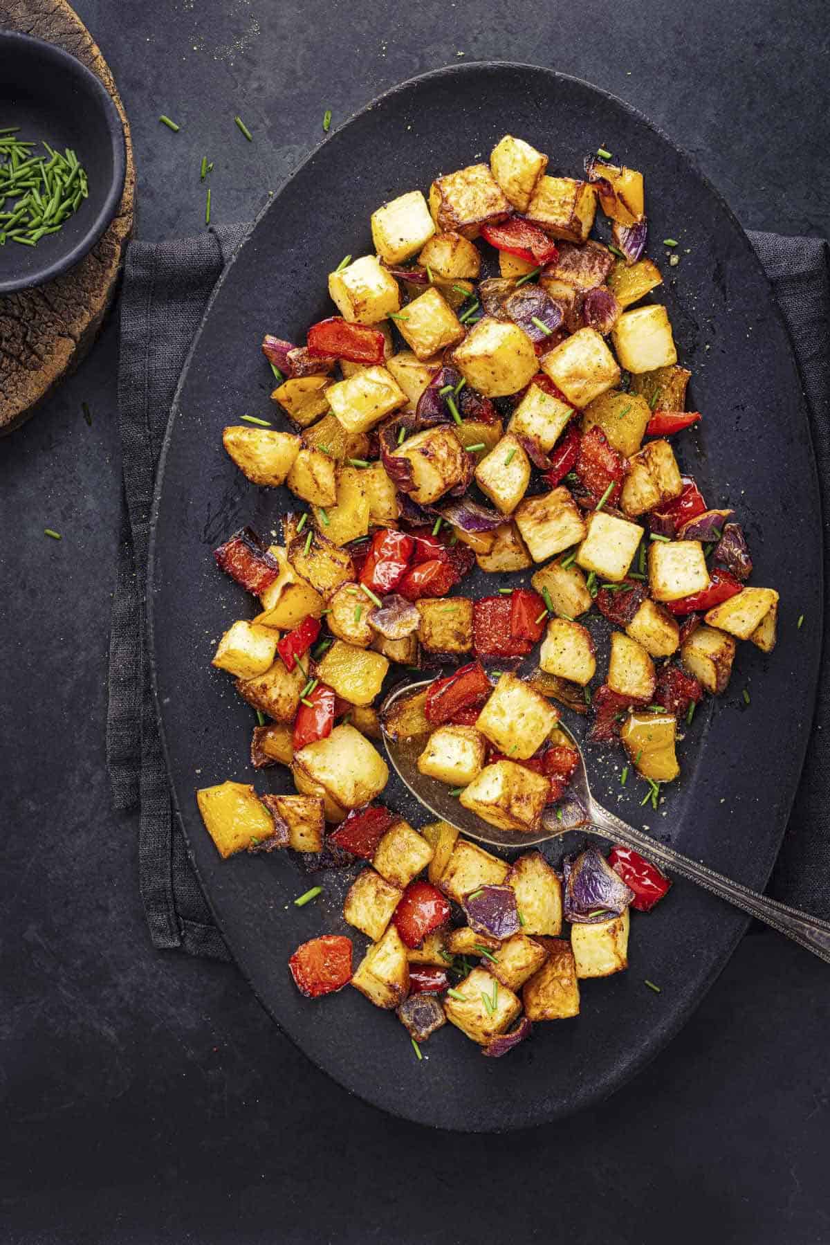 roasted potatoes with onions and peppers in an oval black serving dish.