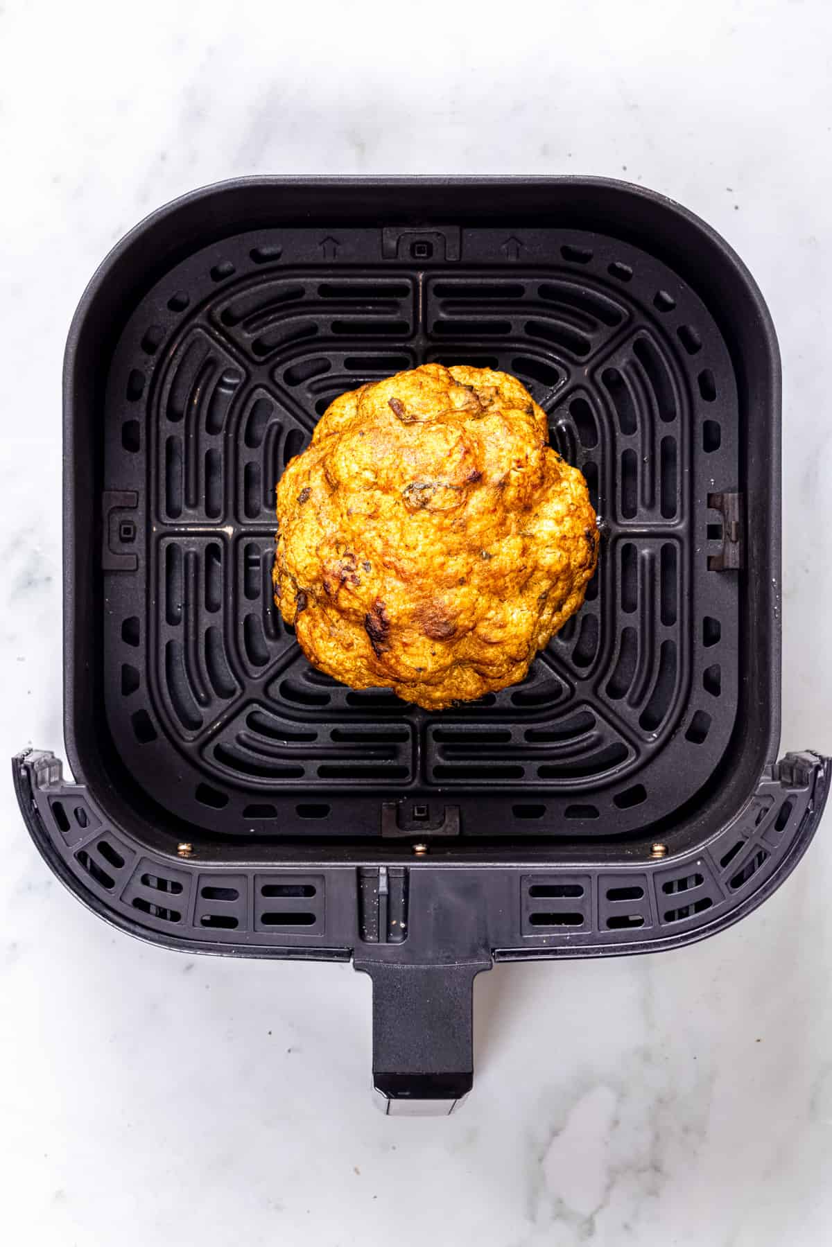 airfried whole cauliflower roasted in air fryer basket.