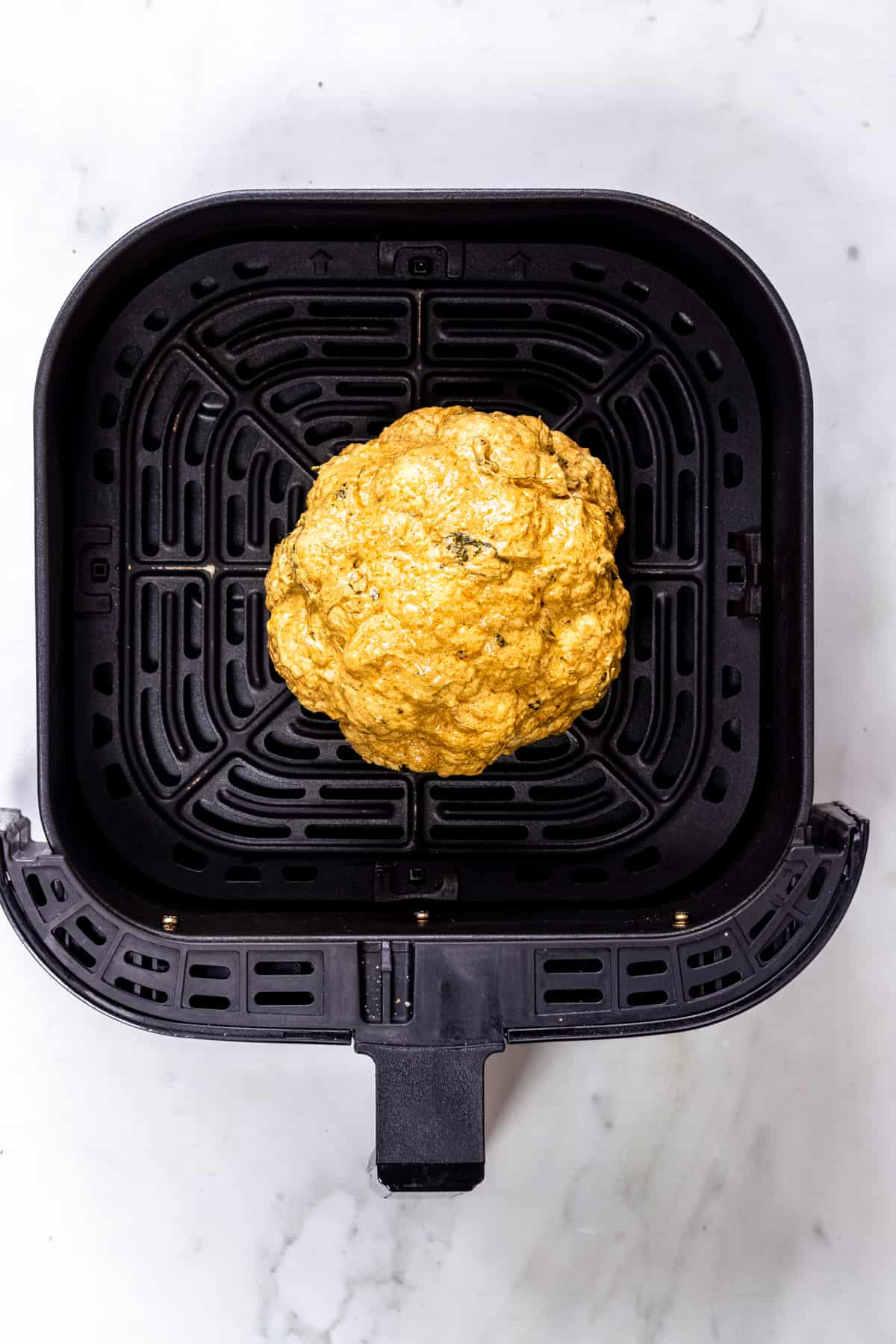 whole cauliflower marinated in an air fryer basket.