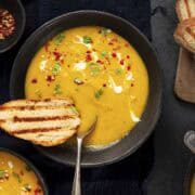 two bowls of carrot coriander soup served with toasted bread.