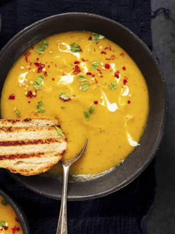 two bowls of carrot coriander soup served with toasted bread.