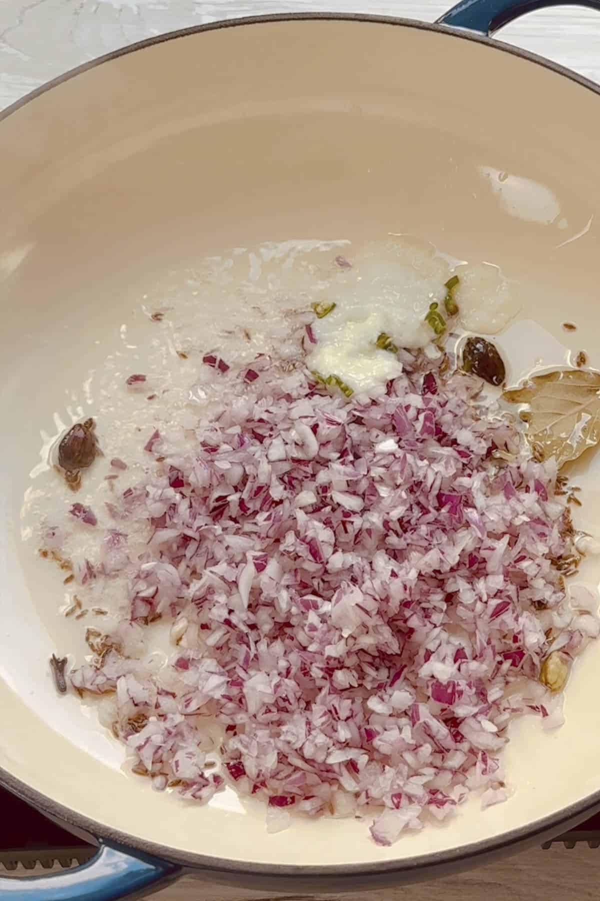 whole spices and diced onion in a pan to make cauliflower and chickpea curry.