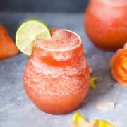 watermelon frozen rose in two glasses served with lime wedges.
