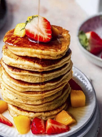 Stack of Mango pancakes with maple syrup and fresh fruits.