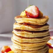 Stack of Mango pancakes with maple syrup and fresh fruits.