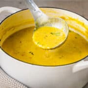 Ladleful of red lentil dal soup and a white pot of soup.