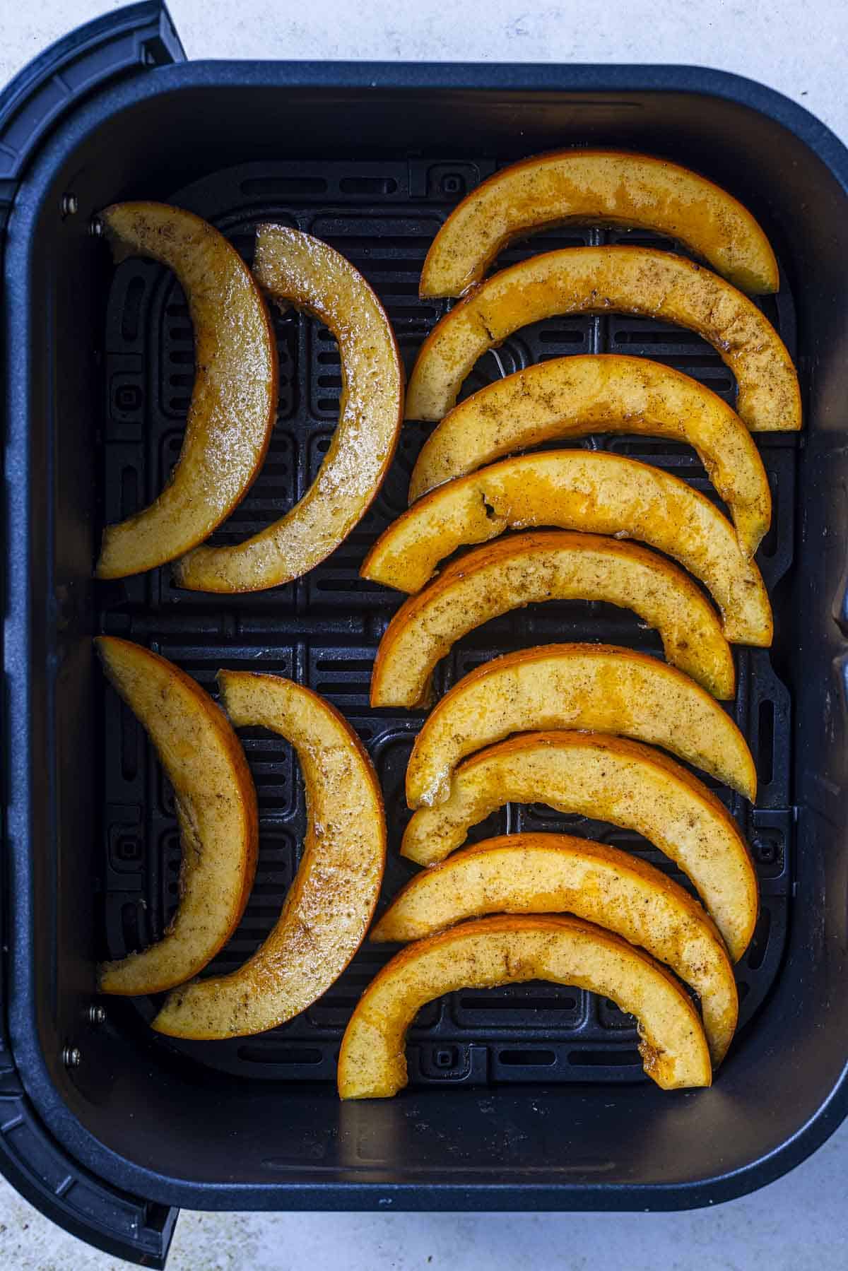 pumpkin slices in an air fryer basket for roasting.