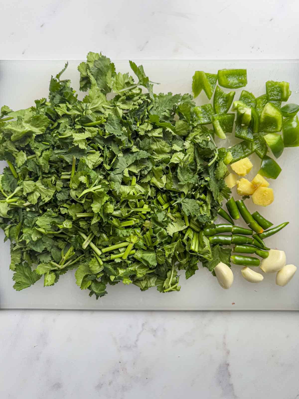 chopped coriander, green chilli, green pepper, garlic and ginger on a chopping board.