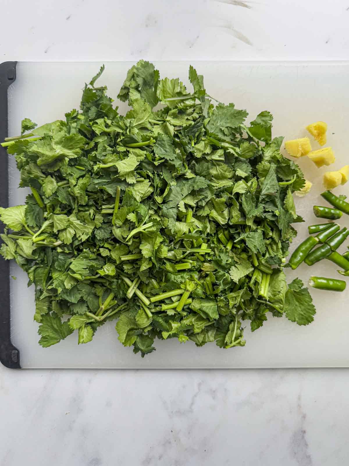 chopped coriander, green chilli and ginger on a chopping board.