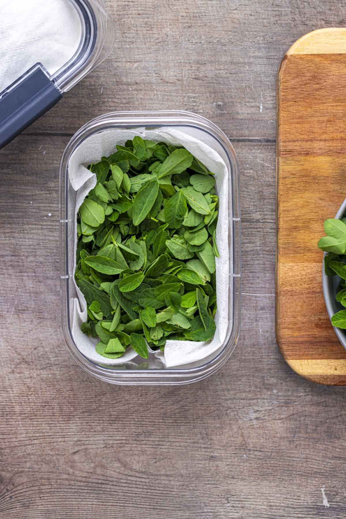 the methi leaves are placed in a plastic box lined with paper.