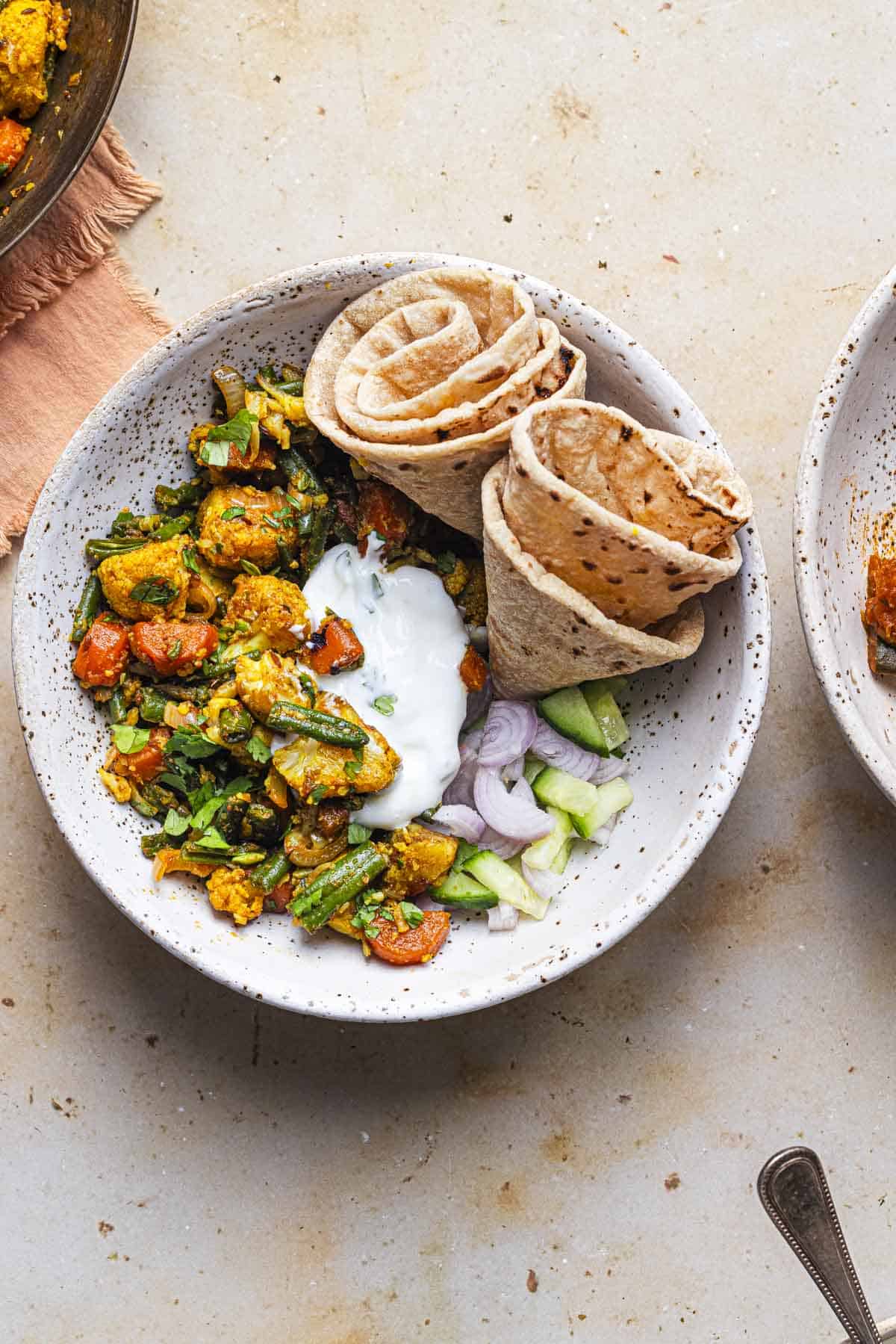 mixed vegetables sabzi served with rotis, yogurt and salad in a bowl.